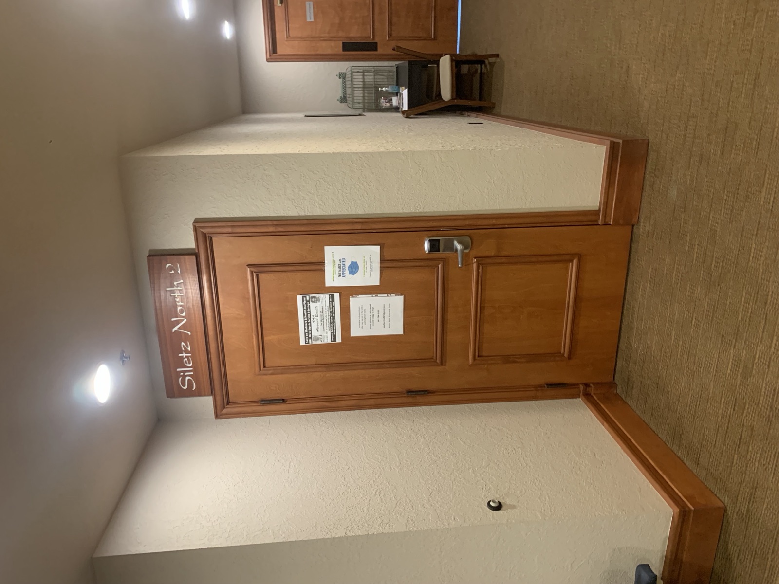 The Advanced Benefits Insurance office door along an interior corridor, under a wooden sign reading Siletz North 2, with notices about Medicare plans and appointments taped to it